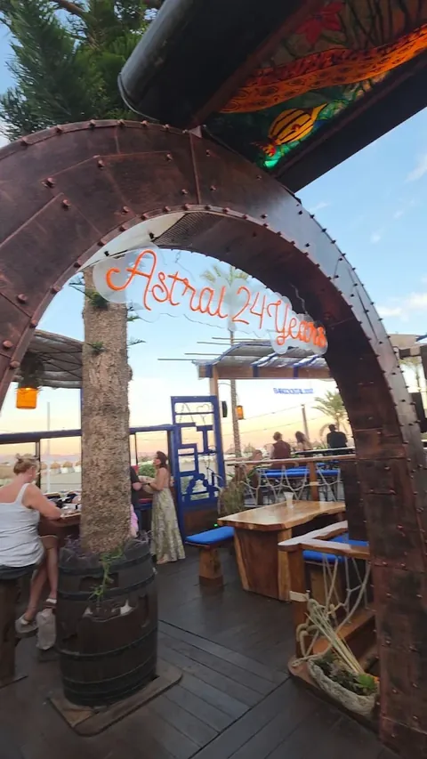 The riveted timber arch on the deck at dusk, with Astral 24 Years written across it in orange neon.