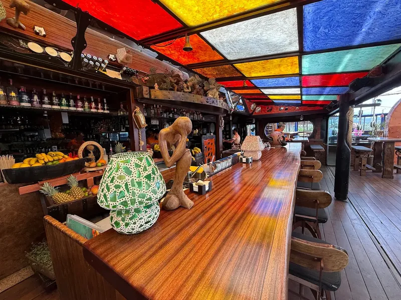 The long mahogany bar inside Astral, lit by a ceiling of red, yellow, blue and green stained glass, with trays of pineapples and bananas behind.