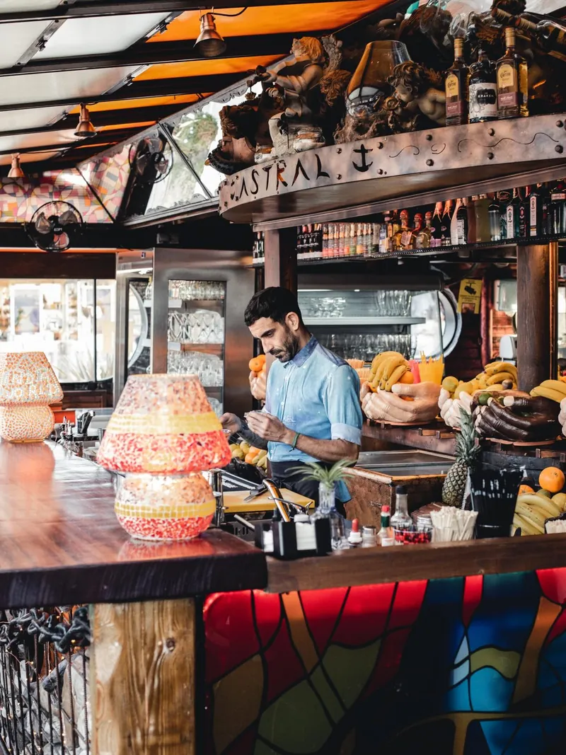 A bartender working behind the Astral bar, surrounded by bananas, pineapples, limes and oranges in carved wooden hands.