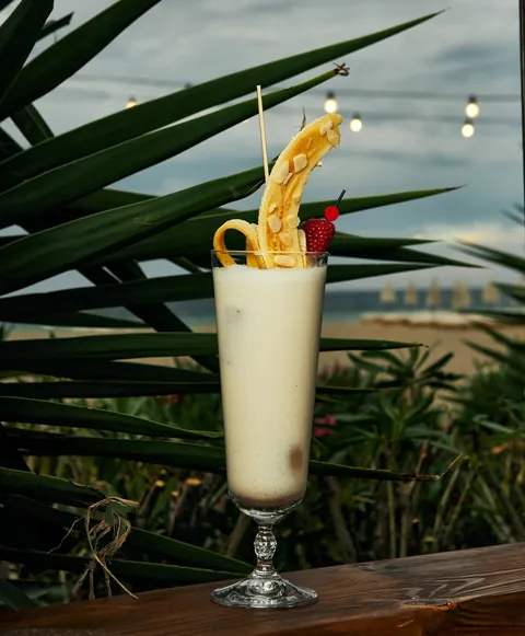 A banana cocktail with the beach and festoon lights behind.