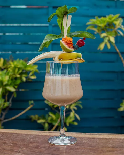 A creamy banana cocktail with mint and marigold against a teal painted wall.