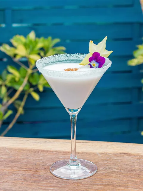 Coconut Martini with a coconut rim, star fruit and a purple viola, against a blue painted wall.