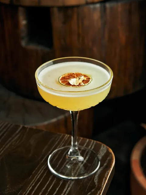 A golden coupe cocktail finished with a dried citrus wheel and edible gold leaf.