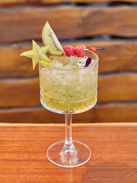 A green cocktail over crushed ice with kiwi, star fruit and raspberries.