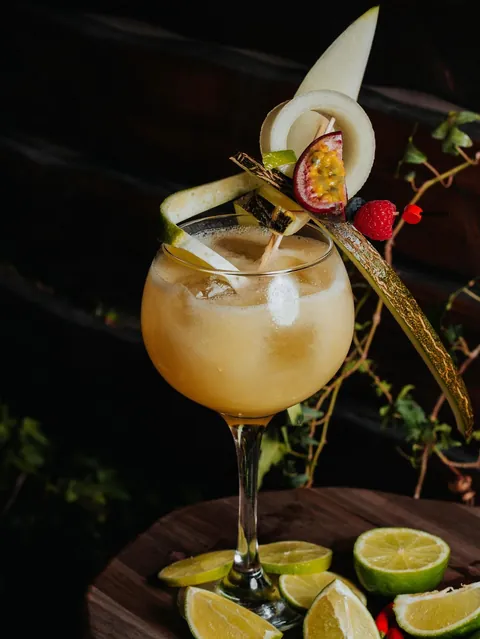 A melon and passion fruit cocktail with a curled melon ribbon and lime peel.