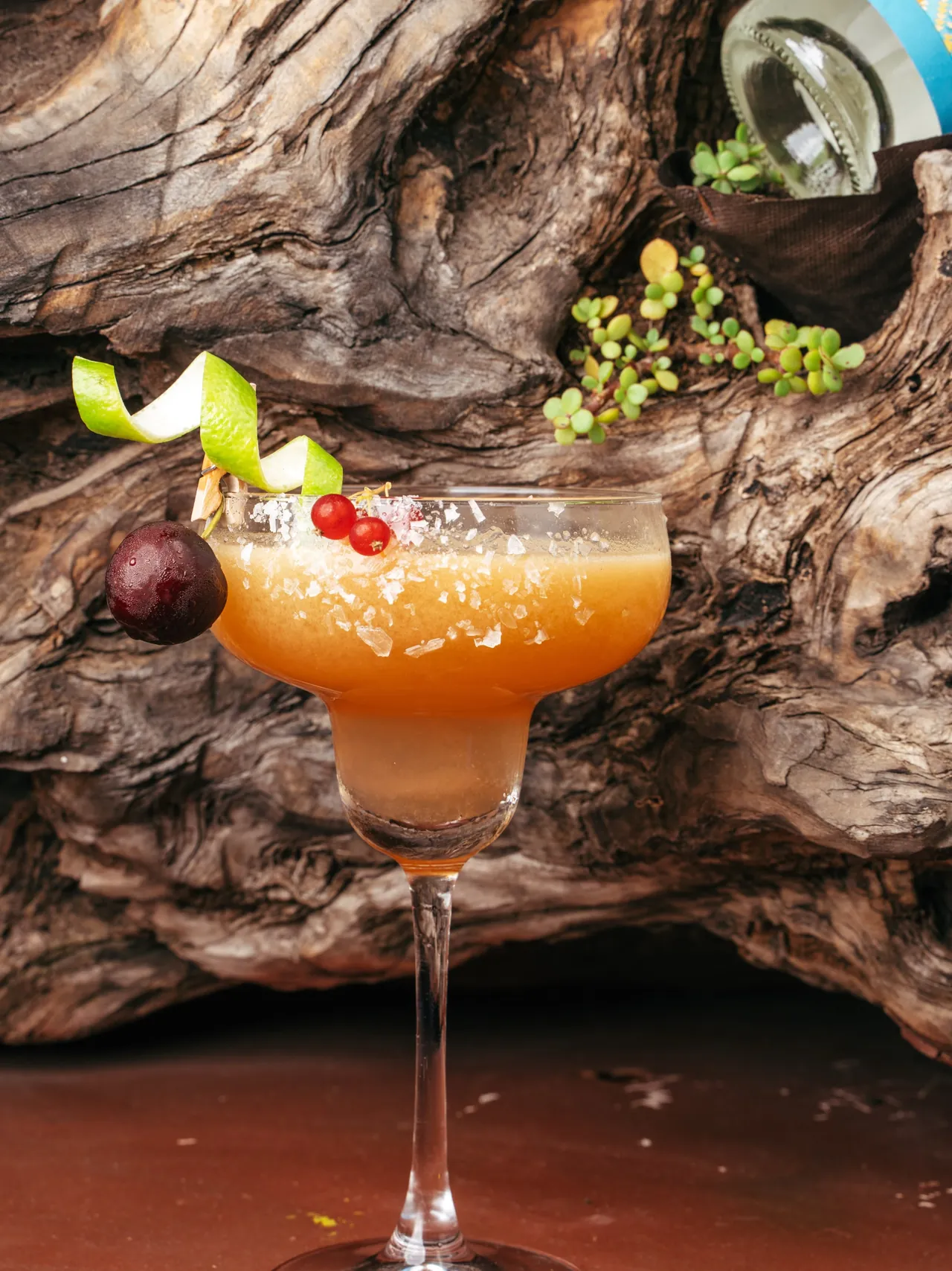 A mezcal margarita with a salt-flake rim, pear and lime twist, plum and redcurrants, against driftwood.
