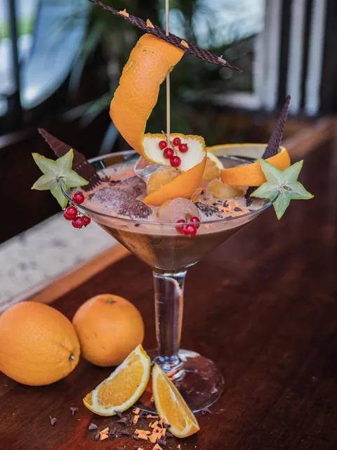 Orange Cookie XXL cocktail in a large martini glass with chocolate shards, star fruit and orange peel.