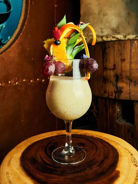 Piña Colada topped with grapes, orange peel, pineapple, raspberry and edible flowers.