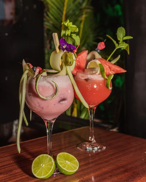 Two pink frozen cocktails with cucumber ribbons and watermelon wedges.