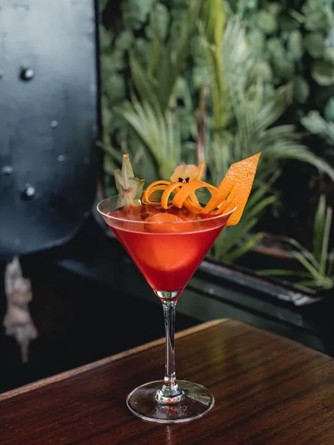 A red martini with orange peel ribbons and a viola.