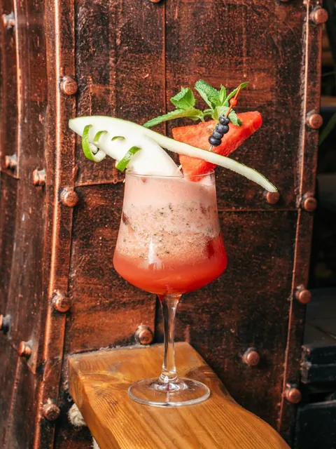 Red Dragon cocktail with watermelon, cucumber ribbon and basil, against the riveted hull of the ship.
