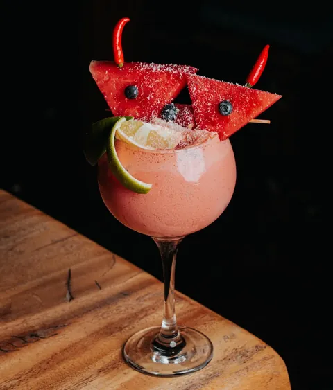 A pink frozen cocktail with coconut-dusted watermelon wedges and two red chillies.