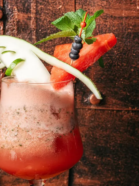 Close-up of a watermelon cocktail with cucumber ribbon, mint and blueberries.