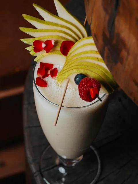 A frozen cocktail crowned with a fan of sliced pear and red rose petals.