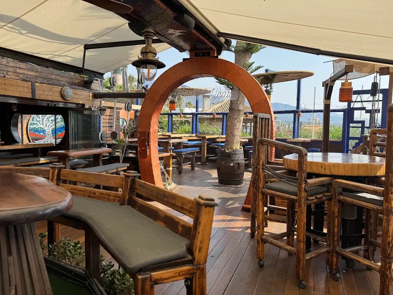 The upper deck in daylight: timber tables, blue railings, cream awnings and a riveted orange arch.