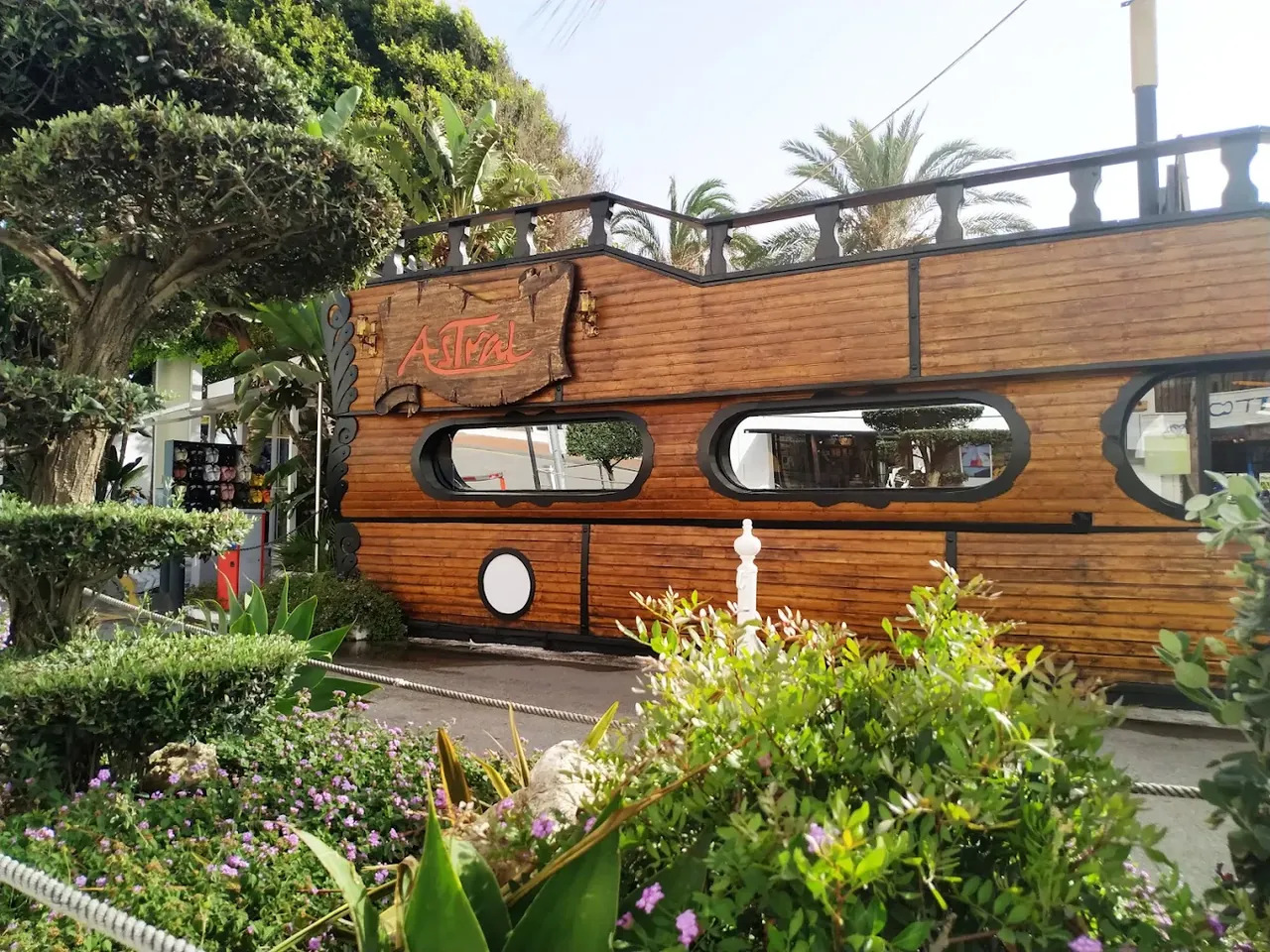 The timber hull of Astral seen from the pavement in Puerto Banús, with the carved name board.