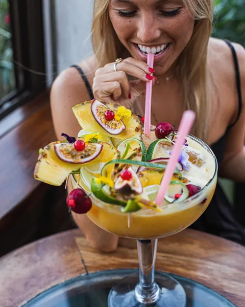 A guest drinking an XXL cocktail stacked with pineapple, passion fruit, lime and cherries.